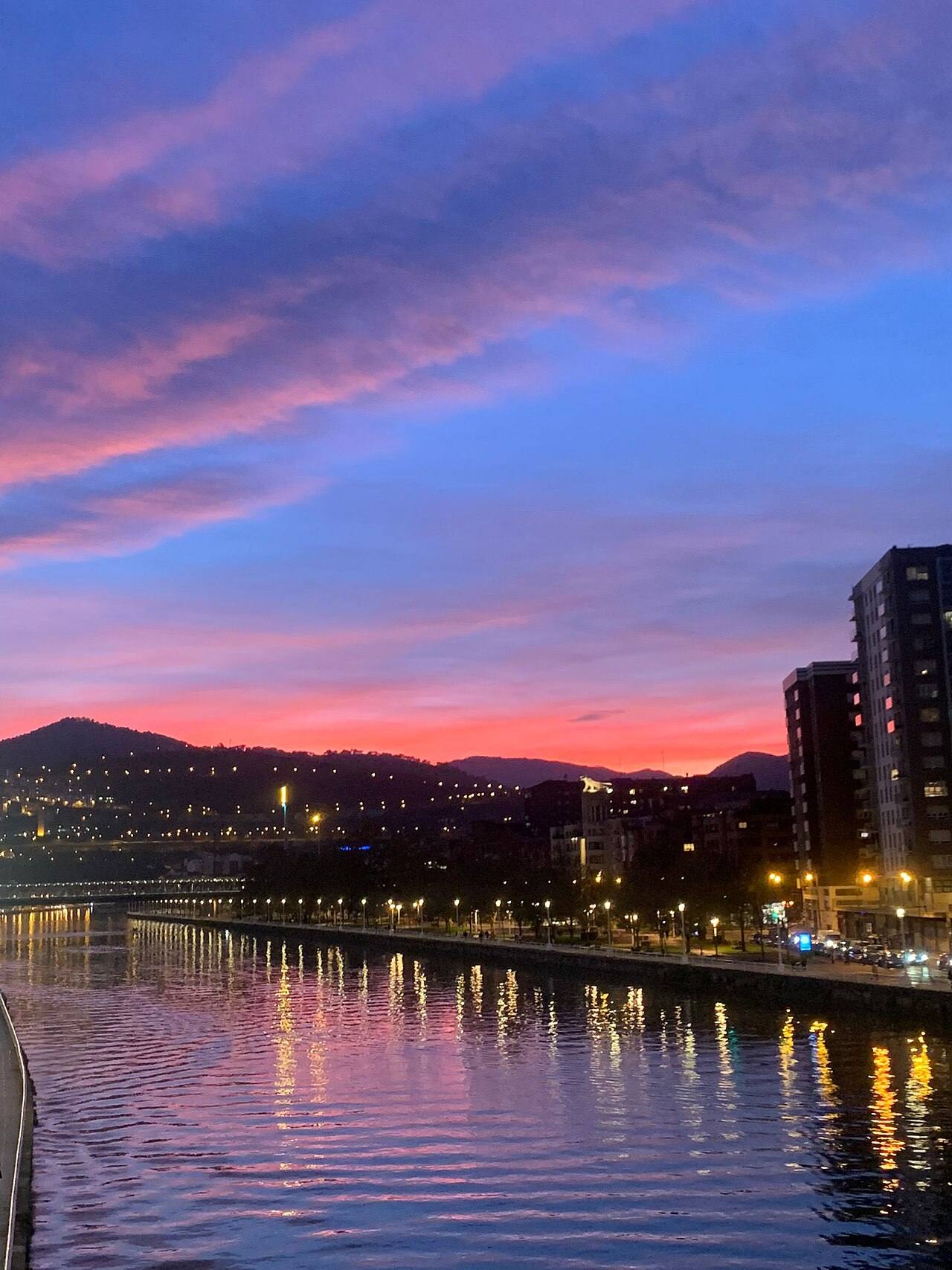 Paseo fluvial junto a la ría de Bilbao al atardecer con edificios iluminados